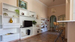 A living room with a TV, white shelves, and a folding chair. - La Dolce Vita - IRIDE's Nest (Roma)