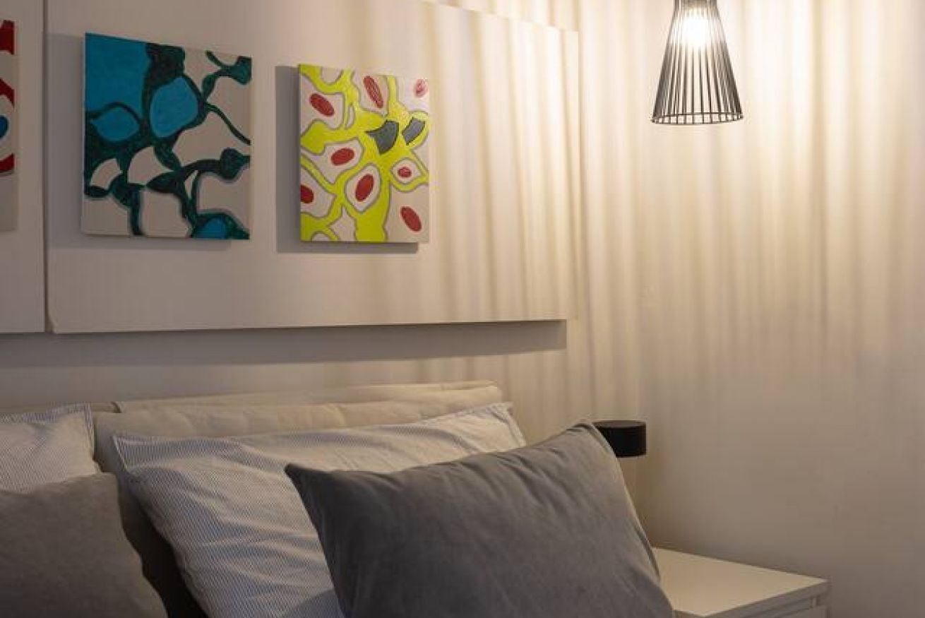Une chambre à coucher moderne avec un lit, des oreillers et une œuvre d’art abstraite au mur.