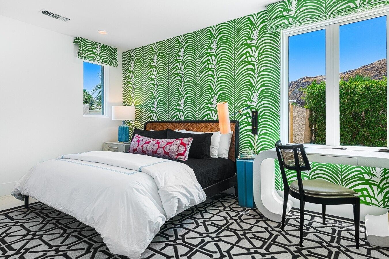 Une chambre avec un lit, une chaise, une fenêtre et un mur décoré de motifs.