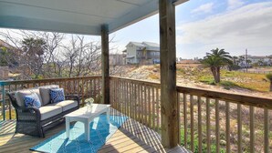 Une terrasse extérieure couverte, dotée d’un canapé et d’une table, qui offre une vue sur un quartier résidentiel avec des maisons et une végétation clairsemée.