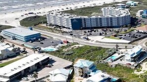 Vue aérienne d’une zone côtière comprenant un grand complexe hôtelier, plusieurs bâtiments plus petits et un parking.