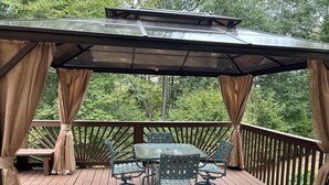 Une terrasse extérieure couverte, dotée d’une table et de chaises, et entourée d’une rambarde en bois et de rideaux.