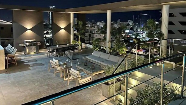 A rooftop terrace with a barbecue, seating area, and a view of the cityscape at night. - Best Apartment in Downtown (Santo Domingo)