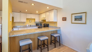 A kitchen with white cabinets, a granite countertop, and three bar stools. - Bear Paw (Flagstaff)