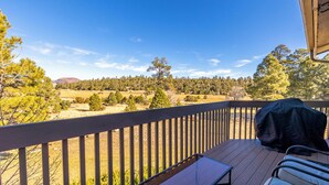 A wooden deck with a barbecue grill, overlooking a scenic landscape with trees and hills. - Bear Paw (Flagstaff)