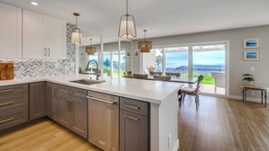 Une cuisine moderne dotée d’un grand îlot central, d’appareils électroménagers en acier inoxydable et de luminaires suspendus.