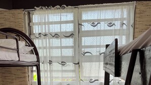 A room with bunk beds, a small round table with a bottle and a cup, and a window with patterned curtains.