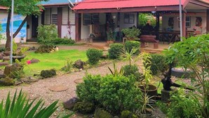A house with a red roof, surrounded by a garden with various plants and rocks.