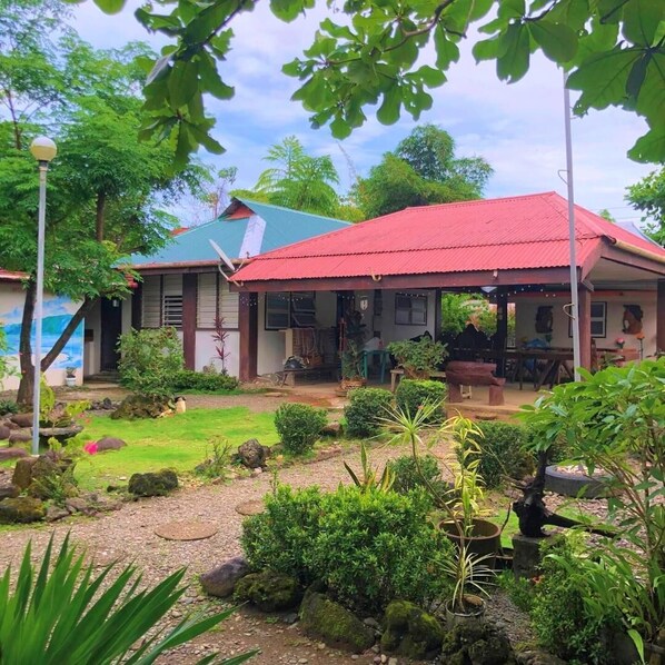 Una casa con techo rojo, rodeada de un jardín con diversas plantas y rocas.