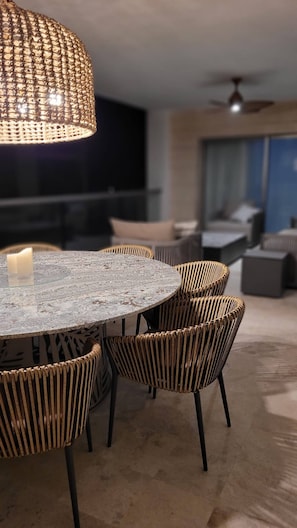 Un coin repas avec une table ronde, des chaises en osier, un luminaire suspendu et un ventilateur de plafond.