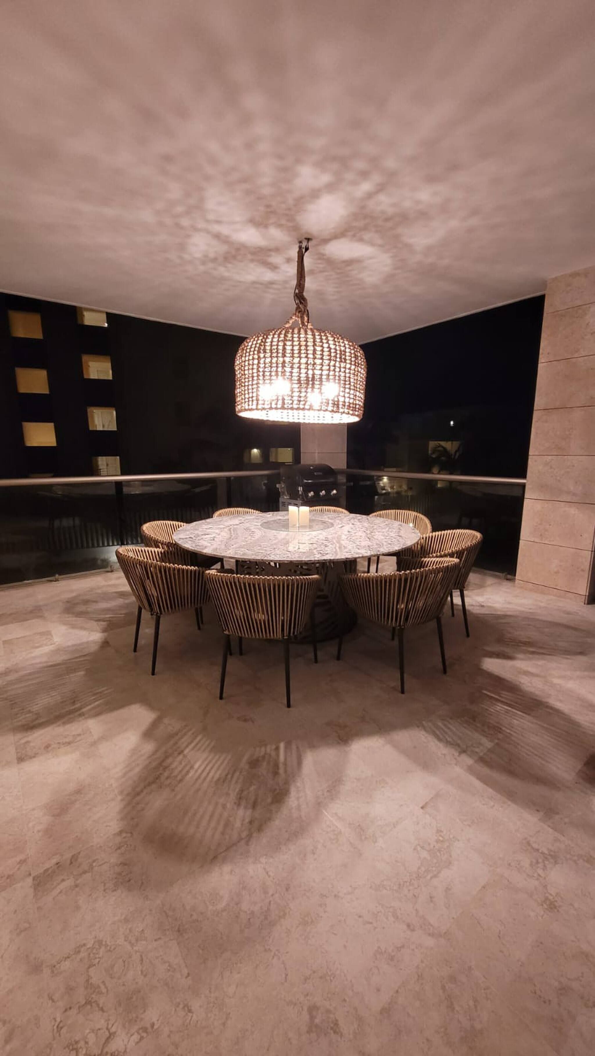 A round dining table with wicker chairs, a glass top, and a central candle.