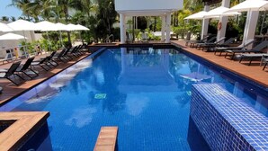 Una piscina con muelle de madera, sillas de descanso, sombrillas y un pabellón.