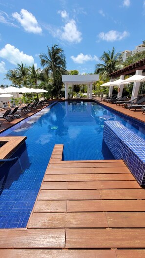 Une piscine avec une terrasse en bois, des chaises longues, des parasols et un kiosque.