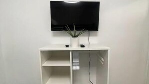 A white entertainment unit with a flat-screen TV mounted above it, a small potted plant, and a power outlet. - Beach Rental 3 Blocks to Beach! WIFI, Cable, A/C, and More! (San Diego)