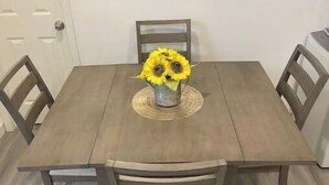 A dining table with four chairs, a vase with sunflowers, and a wooden floor. - Beach Rental 3 Blocks to Beach! WIFI, Cable, A/C, and More! (San Diego)