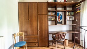 Ein Zimmer mit einem Holzschrank, einem Schreibtisch, einem Stuhl und einem Bücherregal voller Bücher und einem gerahmten Bild.