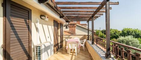Un espacio al aire libre techado con patio, una mesa y sillas, una pérgola de madera y vistas a la vegetación.
