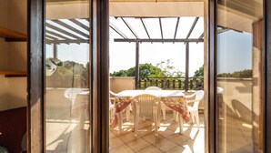 Eine offene Schiebetür führt zu einem Balkon mit Tisch und Stühlen, einer Pergola und Blick ins Grüne.