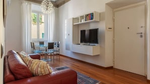 A living room with a sofa, TV, dining table, chairs, and a door.