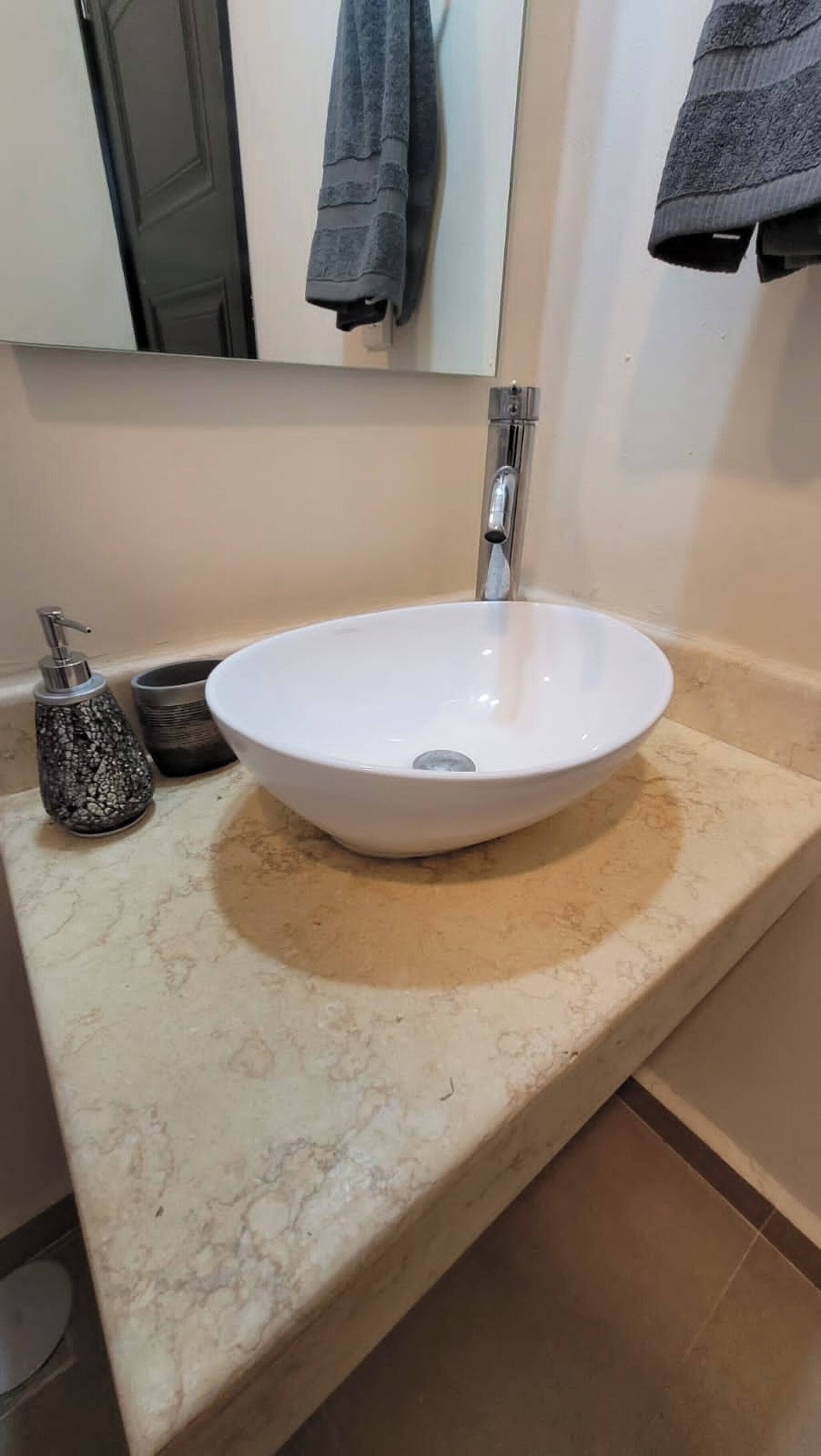 A bathroom with a white sink, a faucet, a soap dispenser, and a towel hanging on the wall.
