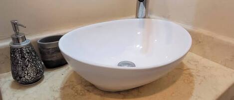 A bathroom with a white sink, a faucet, a soap dispenser, and a towel hanging on the wall.