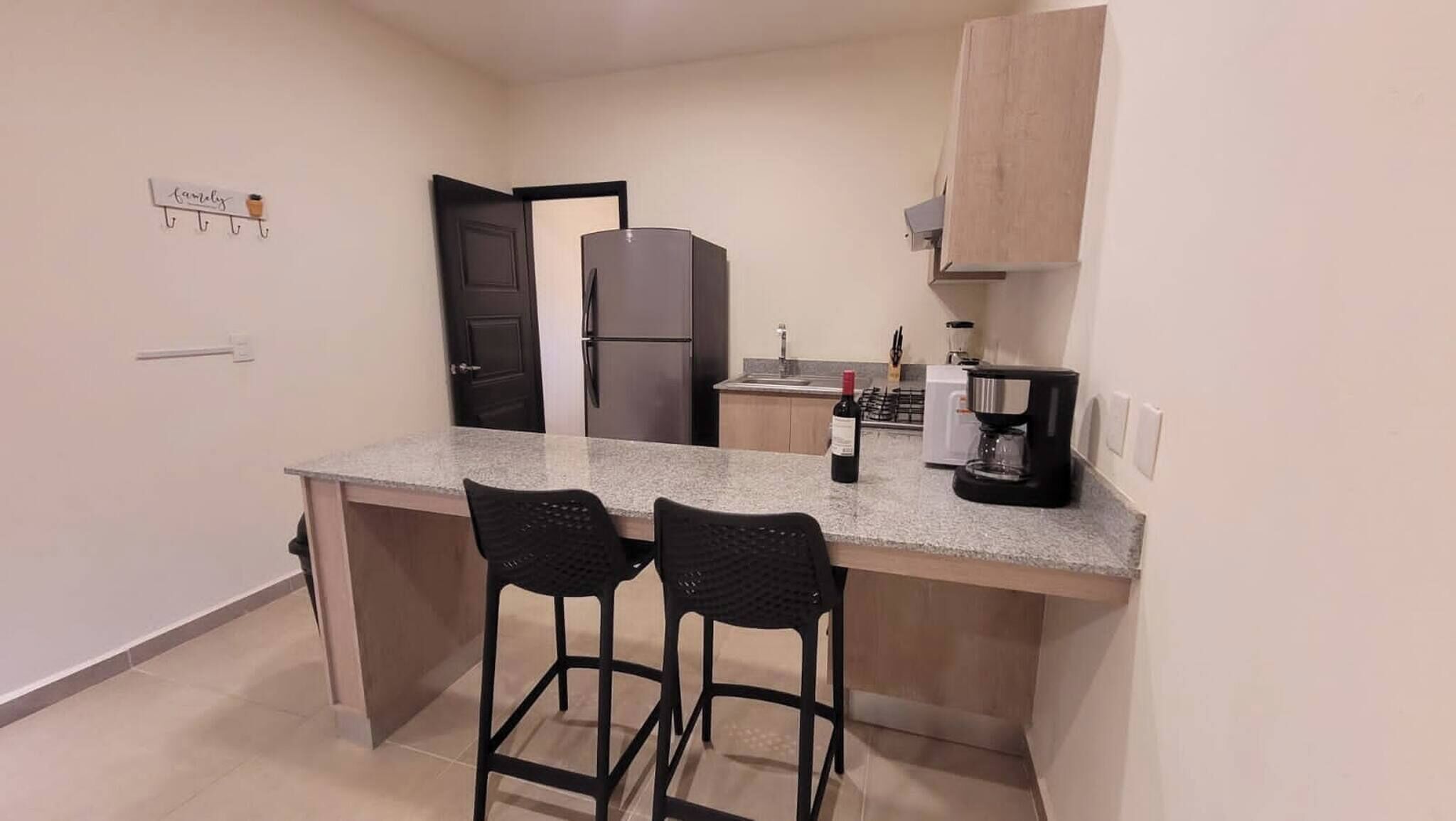 Una cocina pequeña con un refrigerador, una cafetera y dos taburetes de bar.