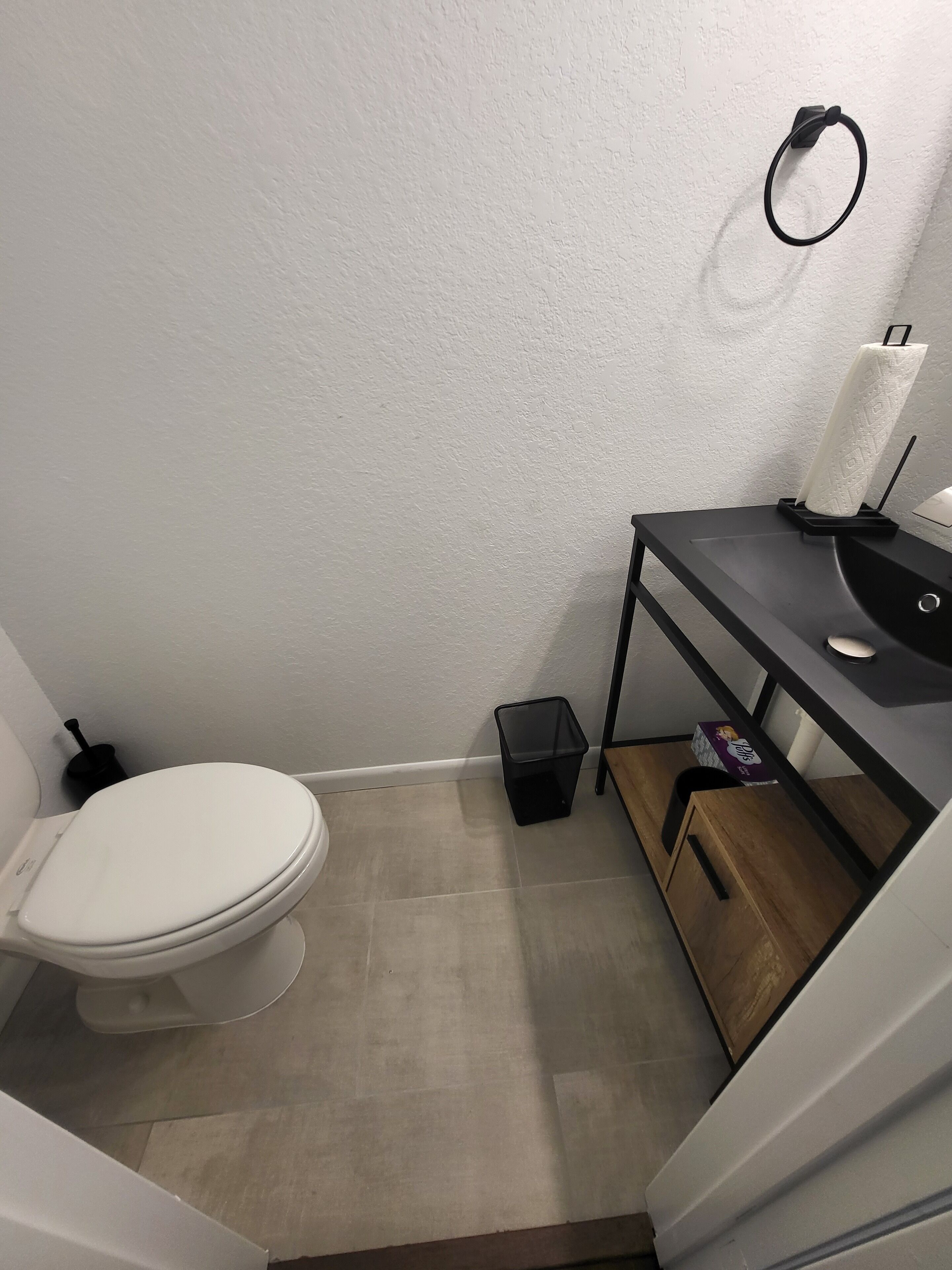 Un baño pequeño con un inodoro, un bote de basura, un dispensador de pañuelos y un armario de madera.