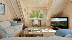 A cozy attic room with a wooden ceiling, a large window, a sofa, a coffee table, and a TV. - Lakefront, Spa, Pool Table, King Beds, Fireplace, Deck, Grill, Private Dock (Big Bear Lake)