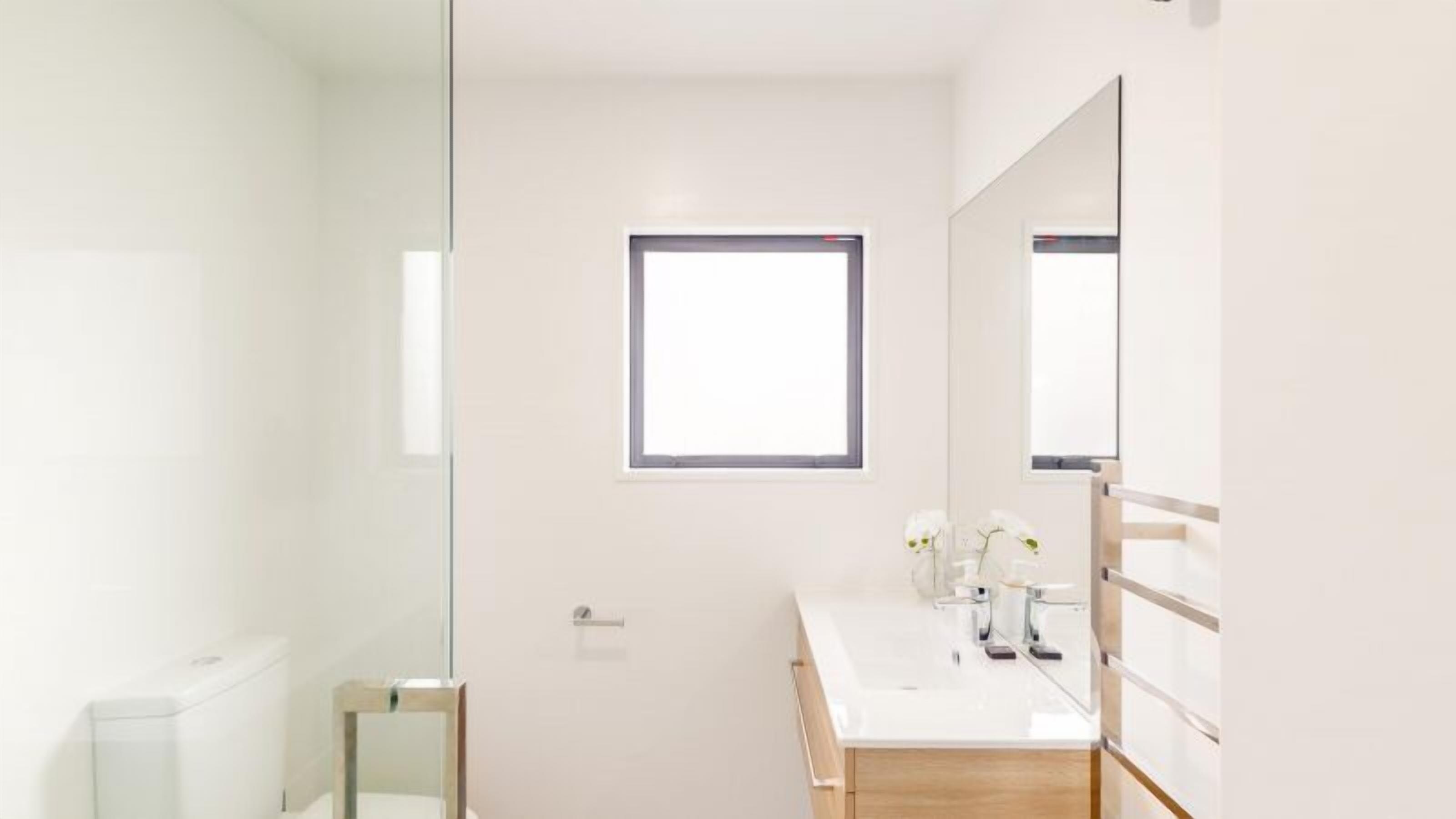 Een moderne badkamer met een grote spiegel, een raam en een wit wastafel.