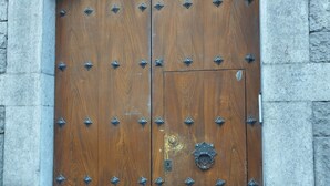 Una puerta de madera grande con tachuelas metálicas y un aldaba en el centro, en una pared de piedra.