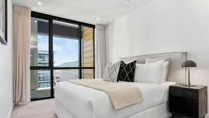 A modern bedroom with a large bed, a nightstand, and a view of the city through a large window. - Sunny and Spacious in Wynyard Quarter (Auckland)