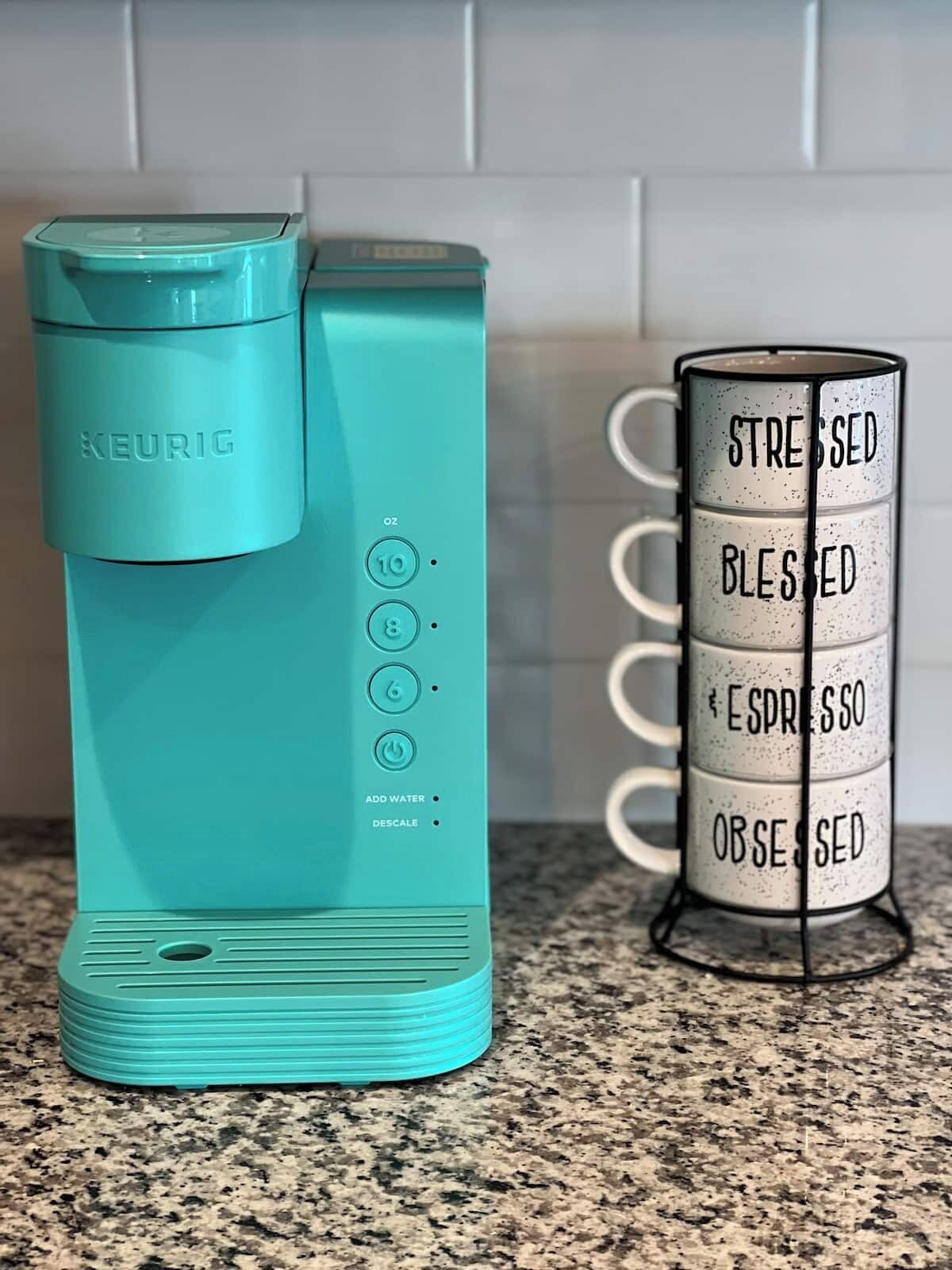 A teal Keurig coffee maker and a mug with motivational phrases.