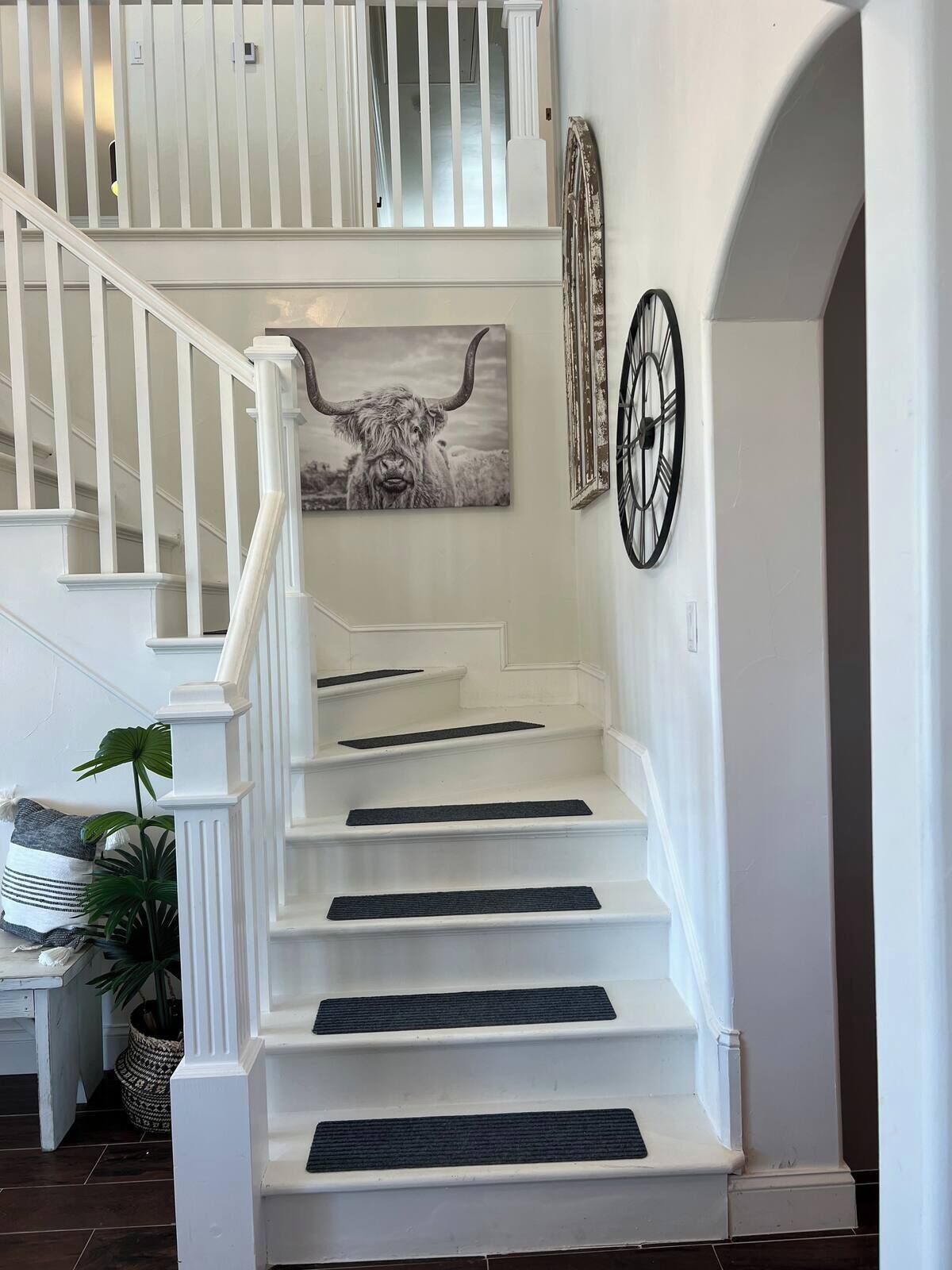 Un escalier blanc avec des marches noires, un tableau représentant un taureau et une horloge au mur.