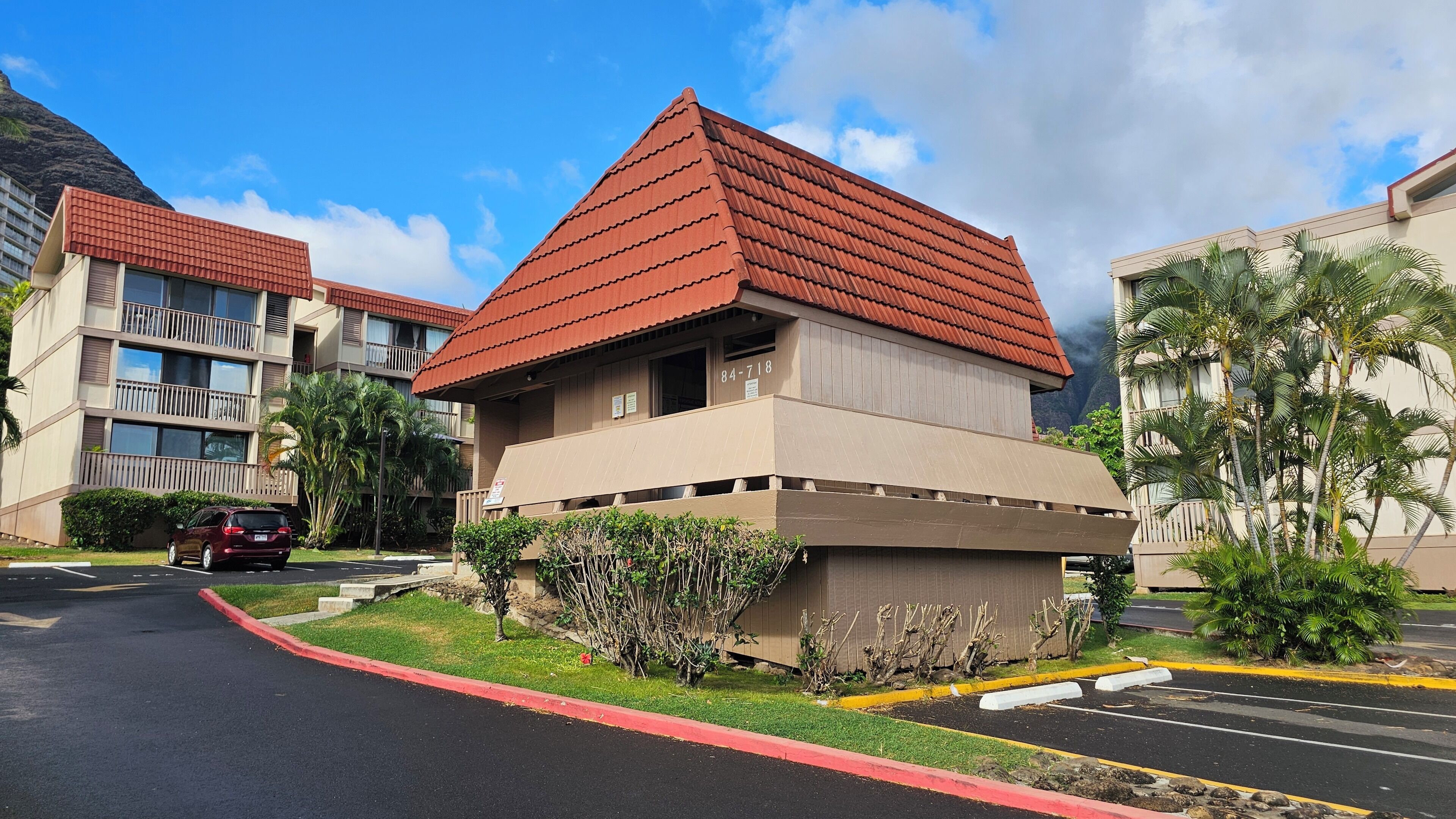 A multi-story building with a red-tiled roof, a parking lot, and surrounding greenery.