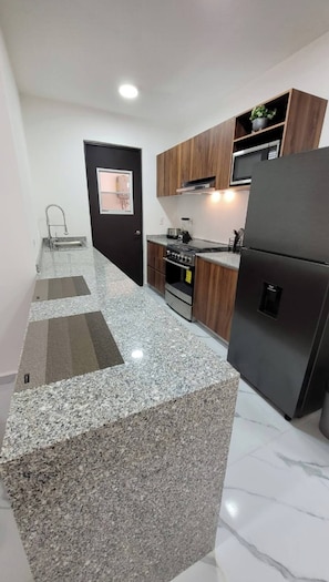 A modern kitchen with granite countertops, a built-in oven, a refrigerator, and wooden cabinets.