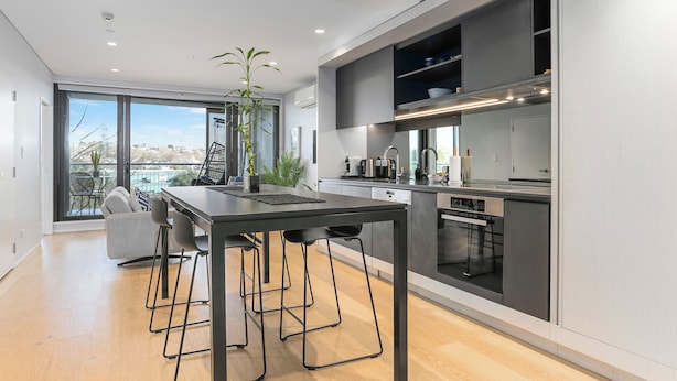 A modern kitchen with a dining area, large windows, and a view of the city. - Light & relaxing on city fringe (Auckland)