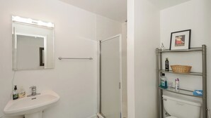 Een badkamer met een wastafel, spiegel, douche en planken met toiletartikelen.