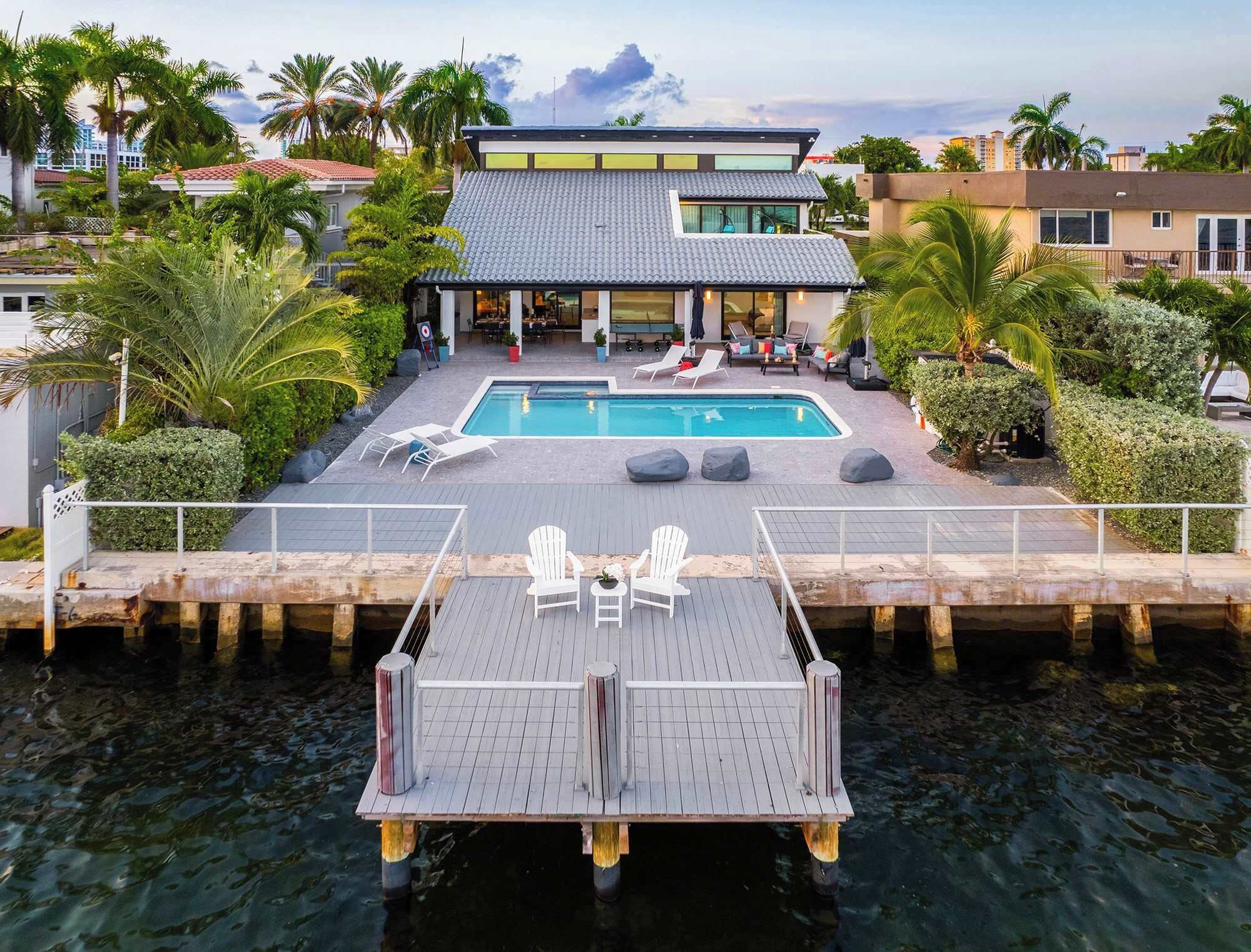 Une maison moderne dotée d’une piscine, de chaises longues et d’une jetée qui s’avance dans l’eau.