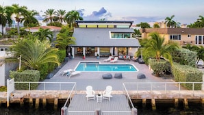 Ett modernt hus med en swimmingpool, solstolar och en brygga som sträcker sig ut i vattnet.