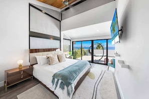 Una camera da letto moderna con un letto grande, un comodino, una TV e un balcone vista mare.
