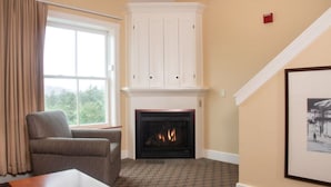A room with a fireplace, a window with curtains, a chair, and a framed picture on the wall.
