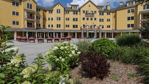 A multi-story hotel with a central courtyard, outdoor seating, and a variety of plants. - Okemo | Charming 1BR Condo + Close to Amenities (Ludlow)