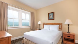 A hotel room with a large bed, two bedside tables with lamps, a nightstand, a window with curtains, and a framed picture on the wall.