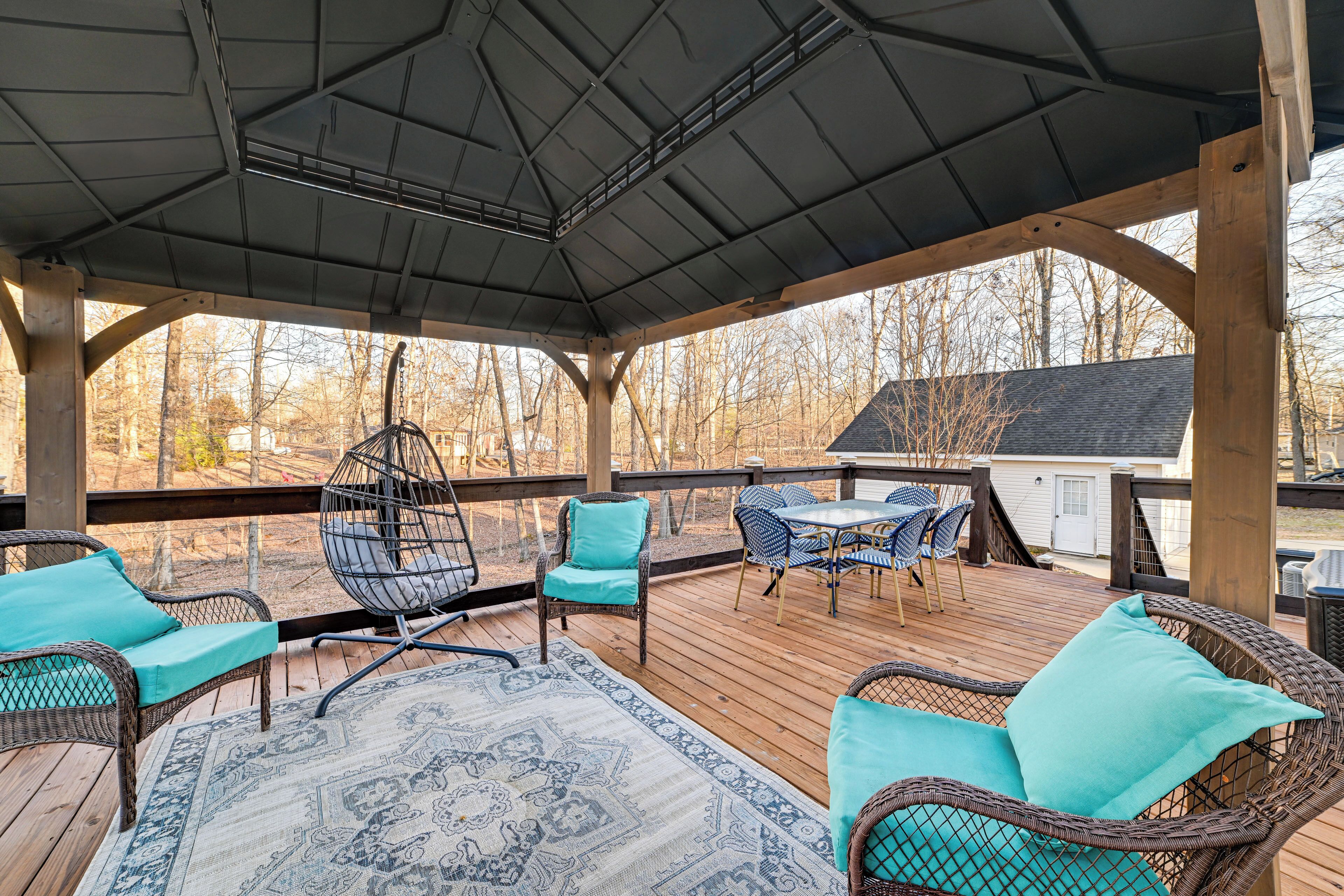 Une terrasse extérieure couverte, aménagée avec des meubles en osier, un tapis à motifs et offrant une vue sur les environs.