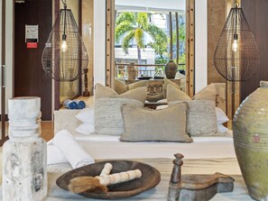 A hotel room with a bed, two hanging light fixtures, a large window with a view of palm trees, and a vase on the side table. - Coastal Luxe at Santai 229 (Tweed)