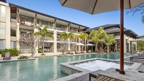 A hotel courtyard with a swimming pool, lounge chairs, and a covered seating area. - Coastal Luxe at Santai 229 (Tweed)