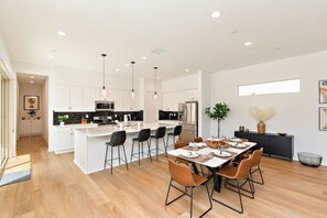 Een moderne keuken met een centraal eiland, barkrukken en een eethoek met een tafel voor vier personen.