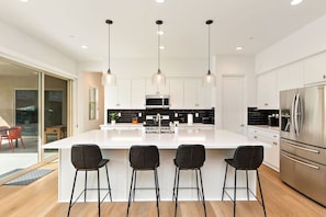 Una cocina moderna con una isla central, electrodomésticos de acero inoxidable e iluminación colgante.