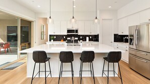A modern kitchen with a large island, stainless steel appliances, and black bar stools. - Palmer Retreat: #260334 3 BR, Pool, Spa, Foosball! (La Quinta)