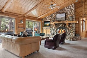L’intérieur d’une cabane en rondins, avec une cheminée en pierre, des meubles en cuir et de grandes fenêtres.